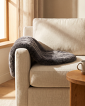 Charcoal faux fur pet mat draped over a cream linen sofa in warm afternoon light