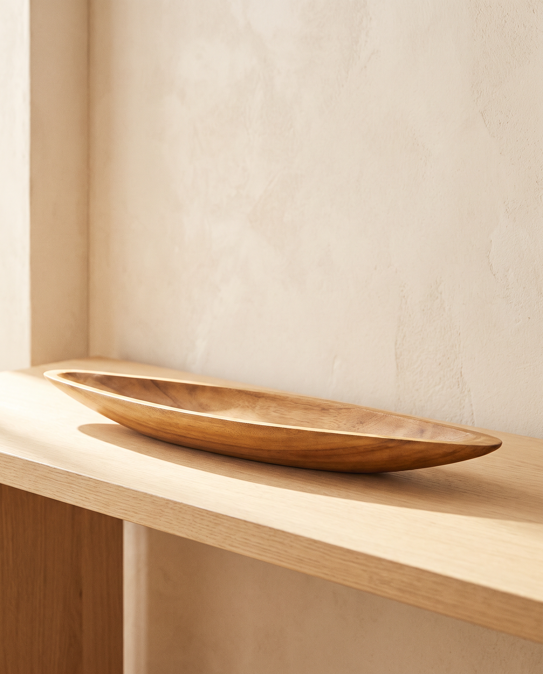 Hand-carved acacia wood boat-shaped tray on a pale oak console in warm light