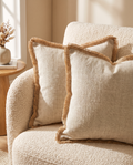 Two linen-trimmed textured cushion covers on a cream boucle armchair in warm light