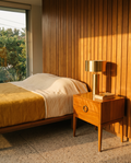 Caramel solid wood nightstand beside a low bed in a warm mid-century bedroom