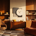Square charcoal and grey wall clock above a teak sideboard